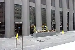 The Sixth Avenue entrances to the CBS Building, looking east. There is a small sculpted sign with Charles Schwab's logo in front of the building's entrances.