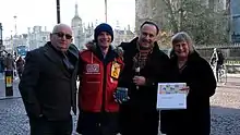 Lord John Bird and Dr Ros Morpeth OBE present bursaries to former and present Big Issue vendors in Trinity Square, Cambridge..